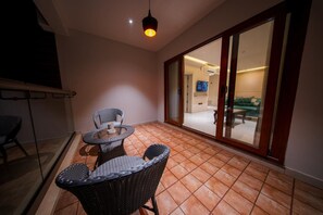 Un balcón con mobiliario de mimbre, una puerta corrediza de vidrio que da a un espacio interior y una lámpara de techo.