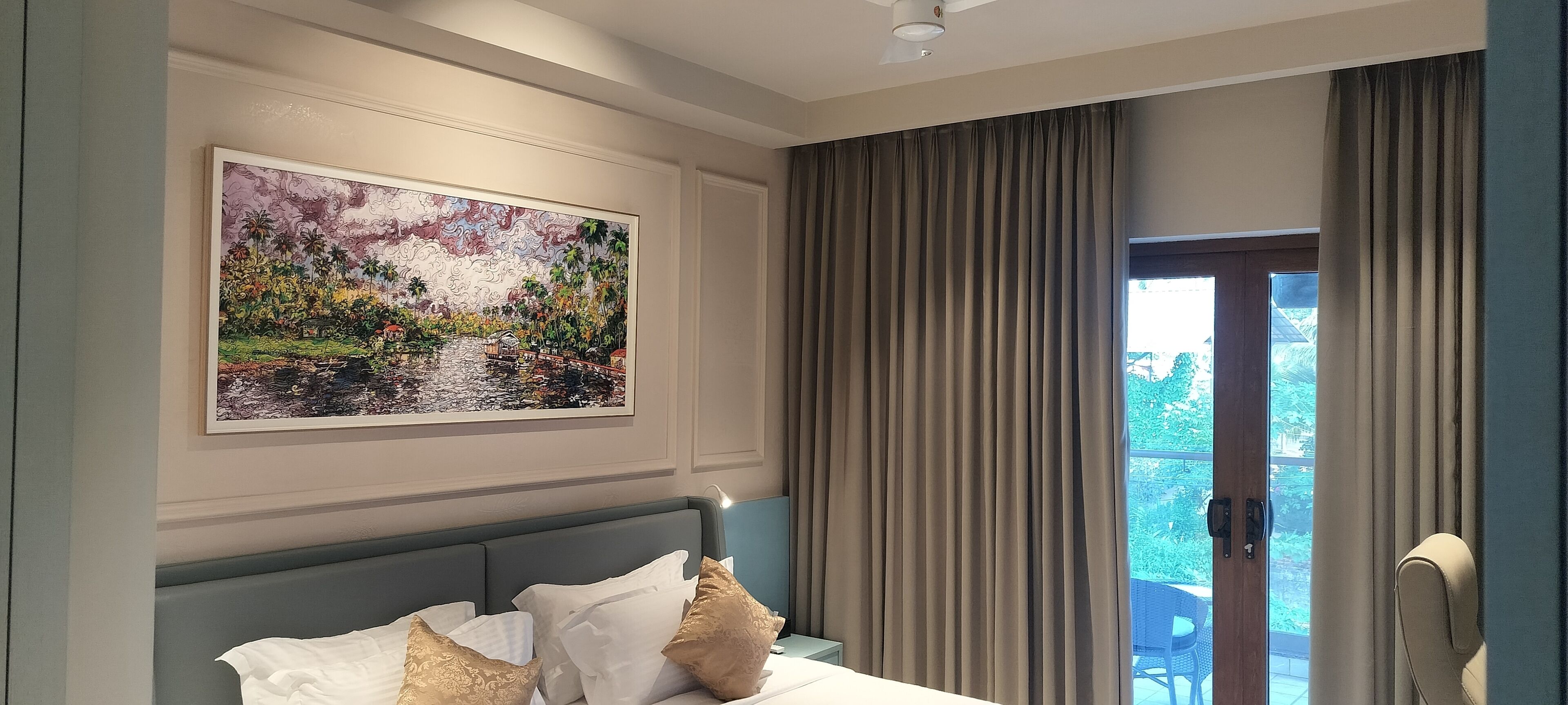 Un cuarto de hotel con una cama, una mesita de noche, una lámpara, un cuadro y vistas a través del ventanal.