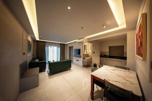 Habitación de hotel moderna con zona de comedor, sofá, televisor y baño.