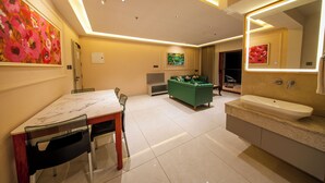 Habitación de hotel moderna con zona de comedor, sofá verde, un cuadro y un espejo grande en el baño.