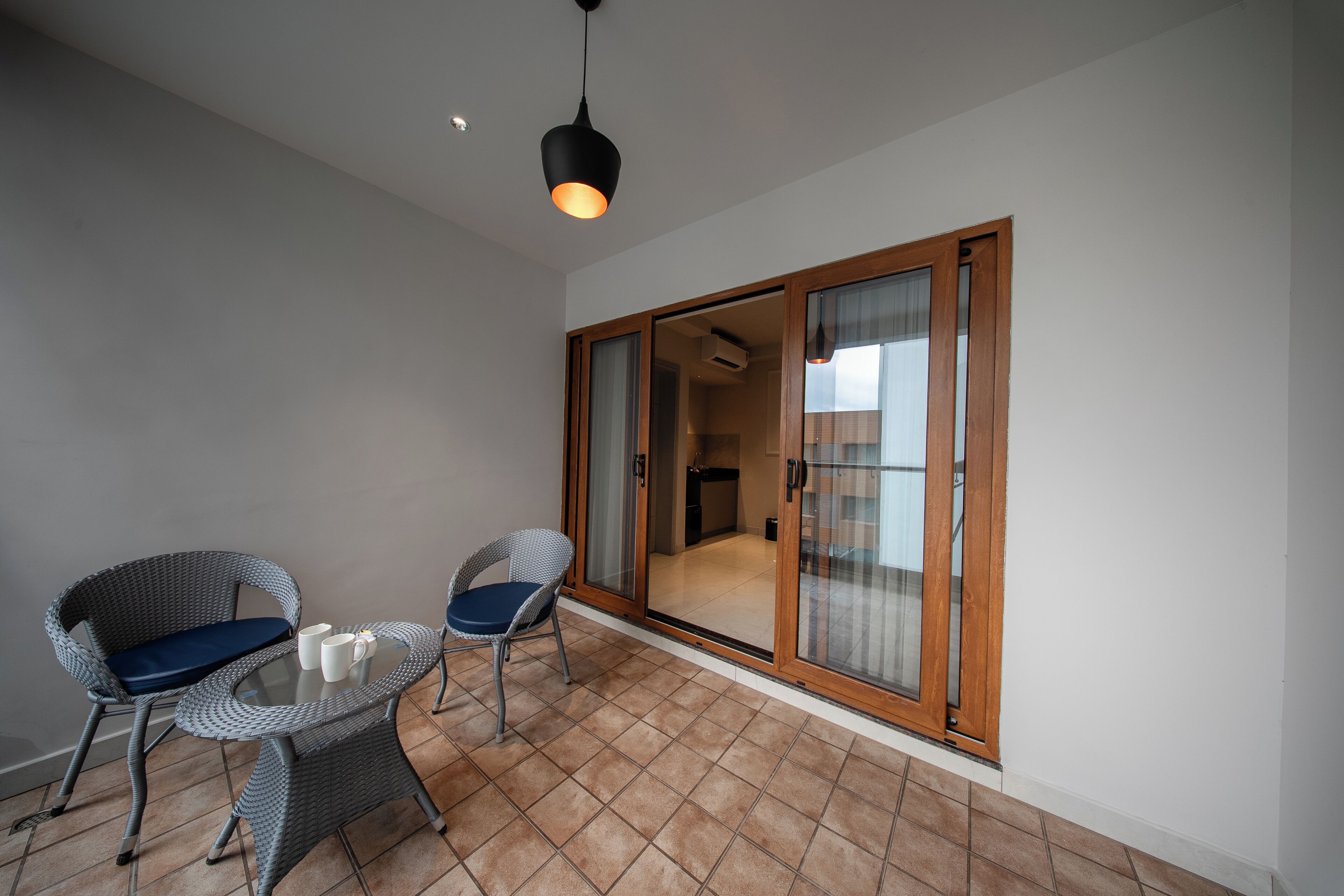 A balcony with two wicker chairs, a glass table, and a hanging light fixture.