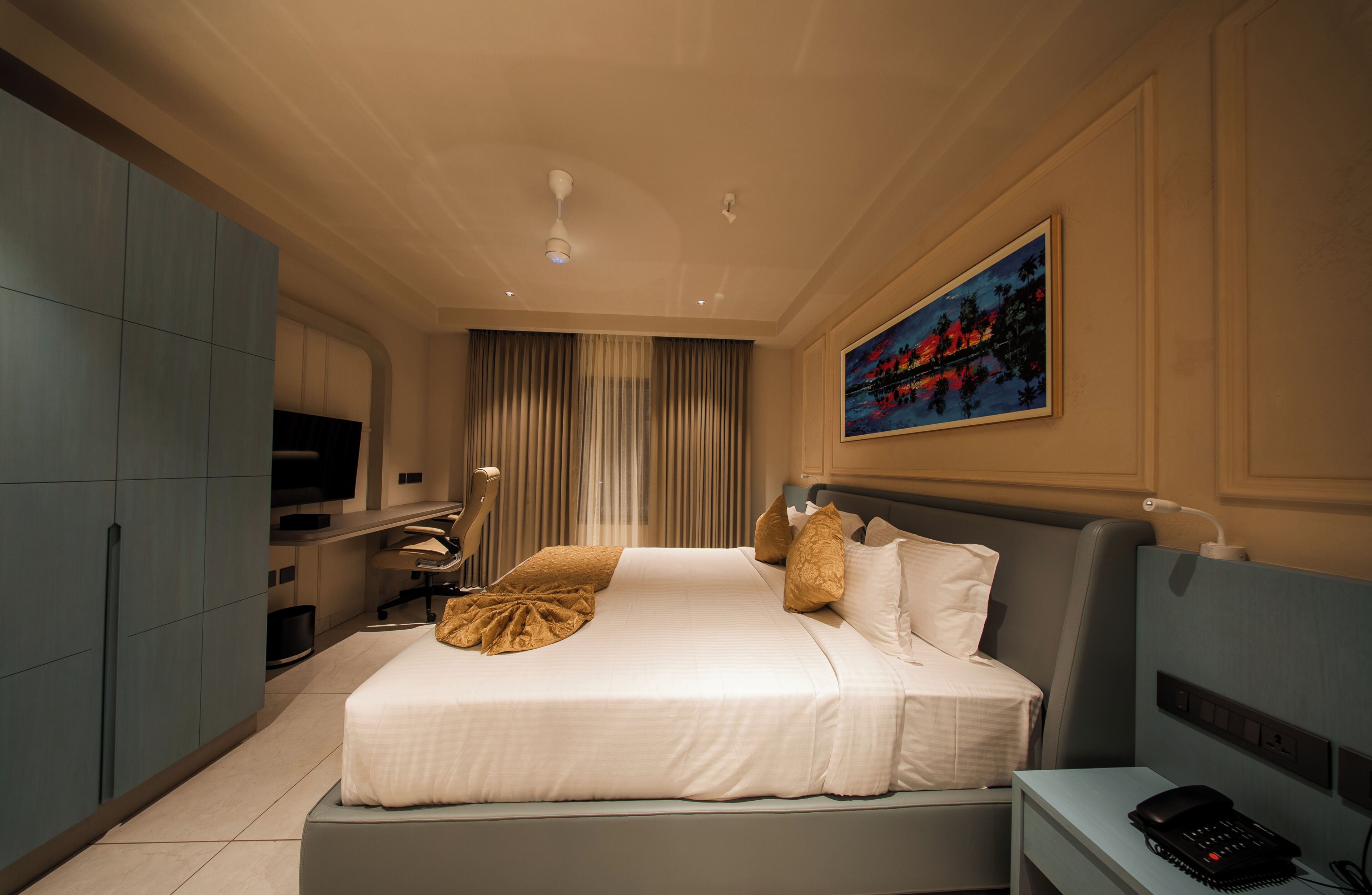 A hotel room with a bed, a desk, a chair, a television, and a painting on the wall.