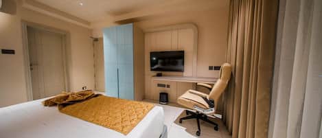 A hotel room with a bed, a desk with a chair, a television, and a window with curtains.