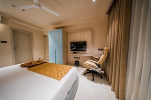 Habitación de hotel con cama, escritorio con silla, televisor y ventana con cortinas.