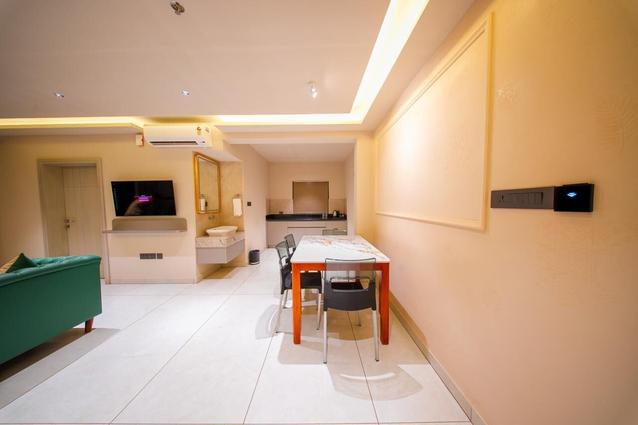 A modern living room with a green sofa, a dining table with chairs, a kitchen area, and a TV.