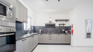 Et moderne køkken med rustfrie apparater, grå skabe og et flisegulv.