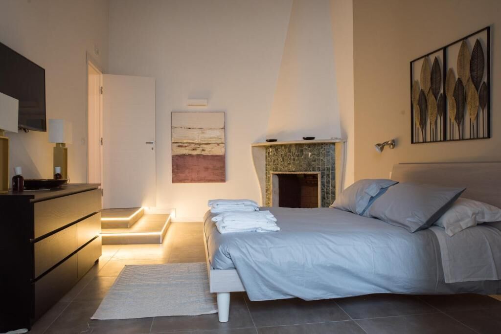 A modern bedroom with a bed, a dresser, a fireplace, and artwork on the walls.