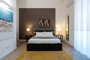 Una camera da letto moderna con un letto grande, due comodini, un'opera d'arte a parete e un'ampia finestra con tende.