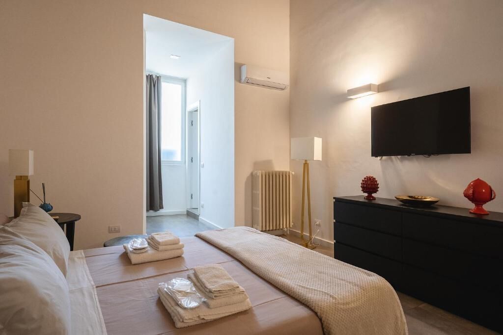 A hotel room with a bed, a TV mounted on the wall, a dresser, and a radiator.