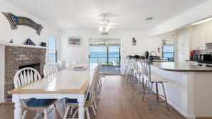 Une cuisine spacieuse avec un grand îlot central, un coin repas agrémenté d’une cheminée en briques et une vue sur l’océan.