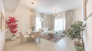 Una sala de estar moderna con un sofá blanco, una mesa de comedor, sillas, una mesa de centro y dos plantas en macetas.