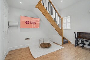 A room with a wooden staircase, a mounted television displaying 'GUEST READY', a round table with a glass top, and a white rug on the floor. - Guestready - Duke Street (Liverpool)