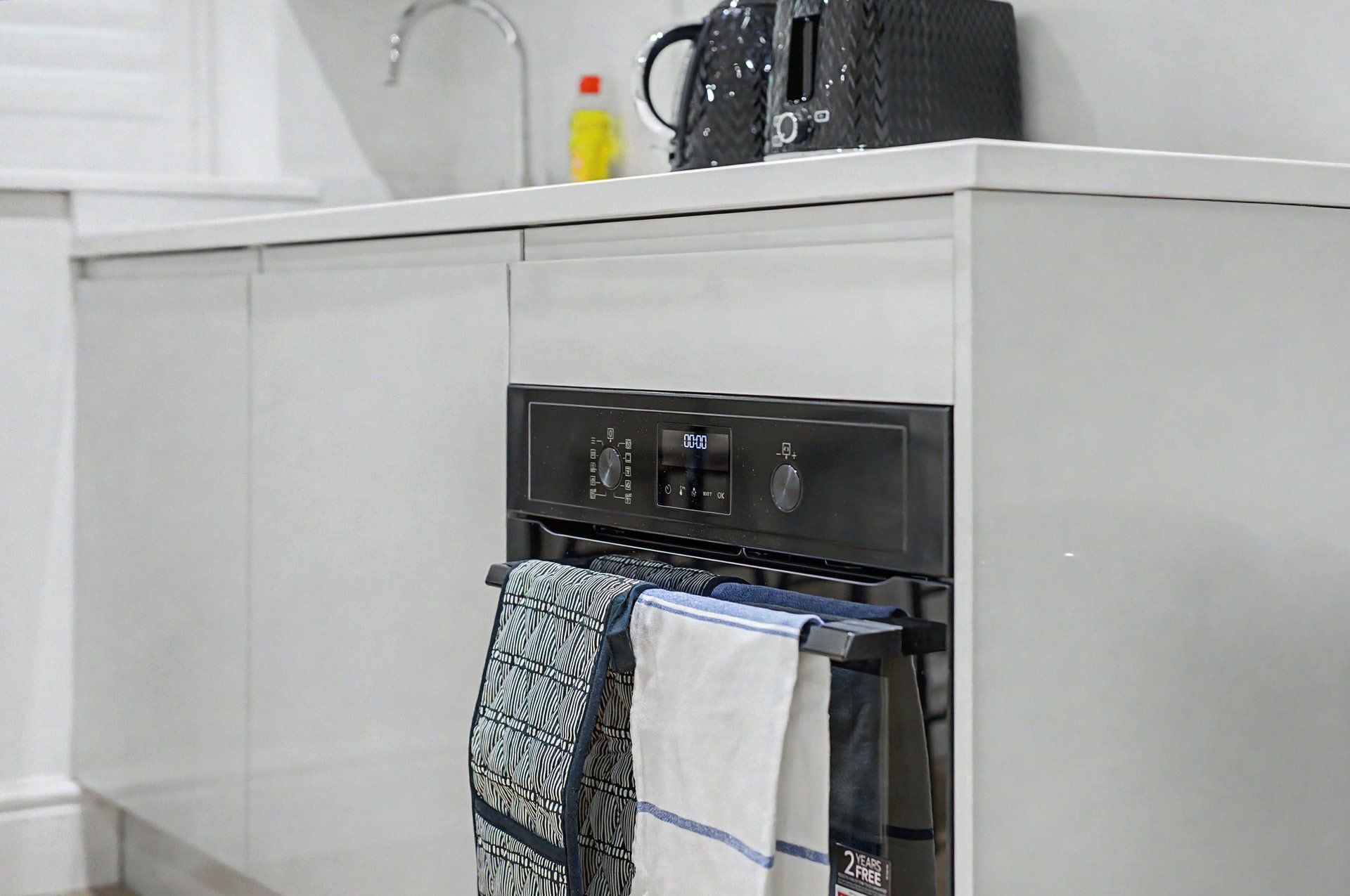 A kitchen with a built-in oven, a digital control panel, and a towel rack with patterned towels.