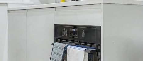 A kitchen with a built-in oven, a digital control panel, and a towel rack with patterned towels.