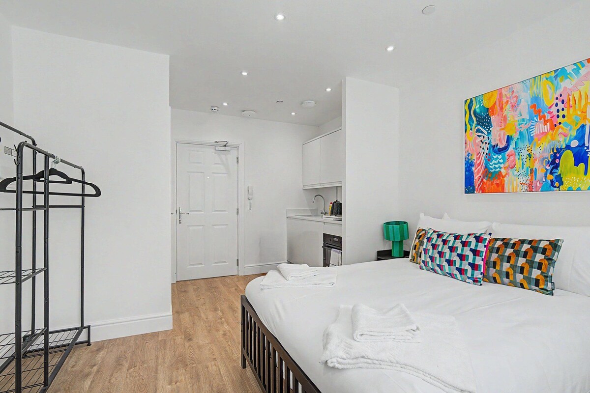 A hotel room with a bed, a wardrobe, a bathroom, and a colorful abstract painting.