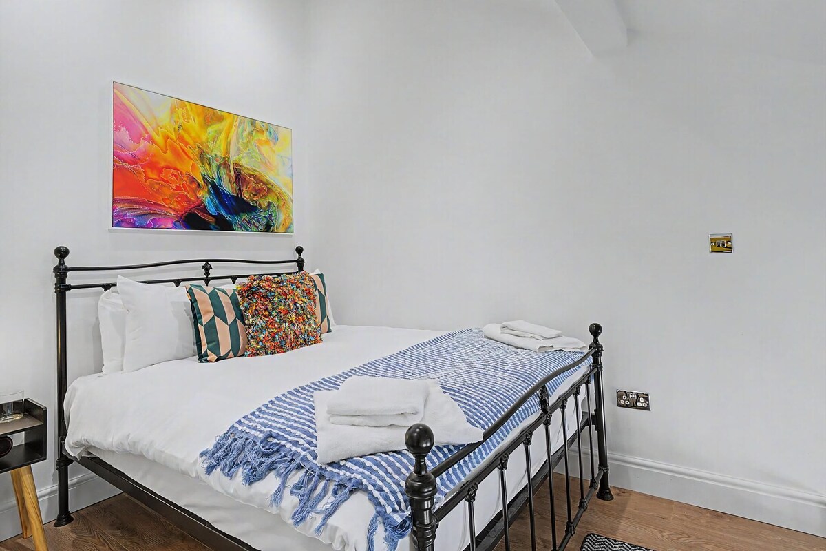 A bed with a blue and white striped blanket, white pillows, and a colorful abstract painting above it.