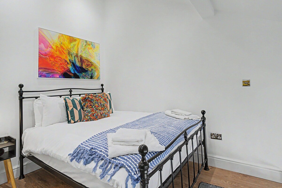 A neatly made bed with a blue and white striped blanket, a colorful pillow, and a white pillow.
