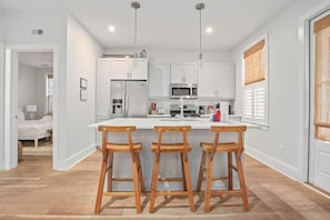 Una cocina moderna con armarios blancos, una isla central con taburetes y un microondas.