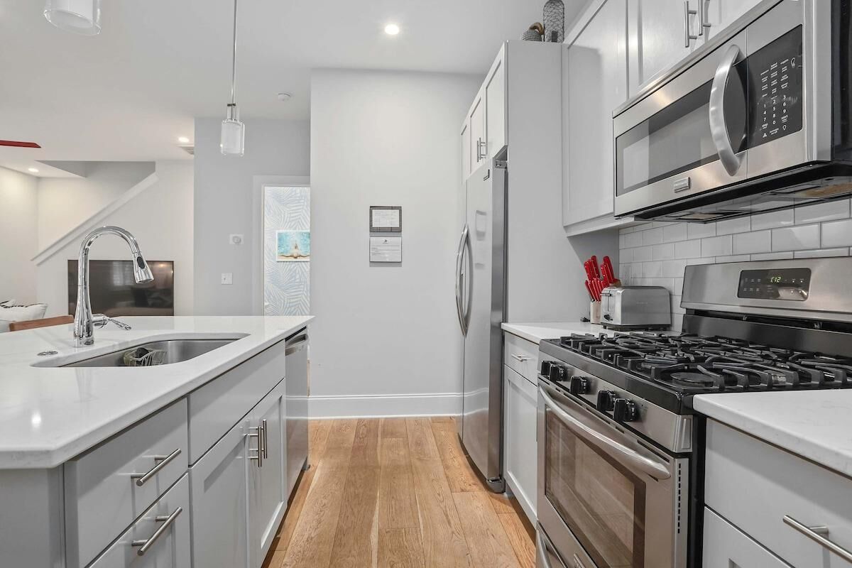 A modern kitchen with white cabinetry, stainless steel appliances, and a wooden floor.