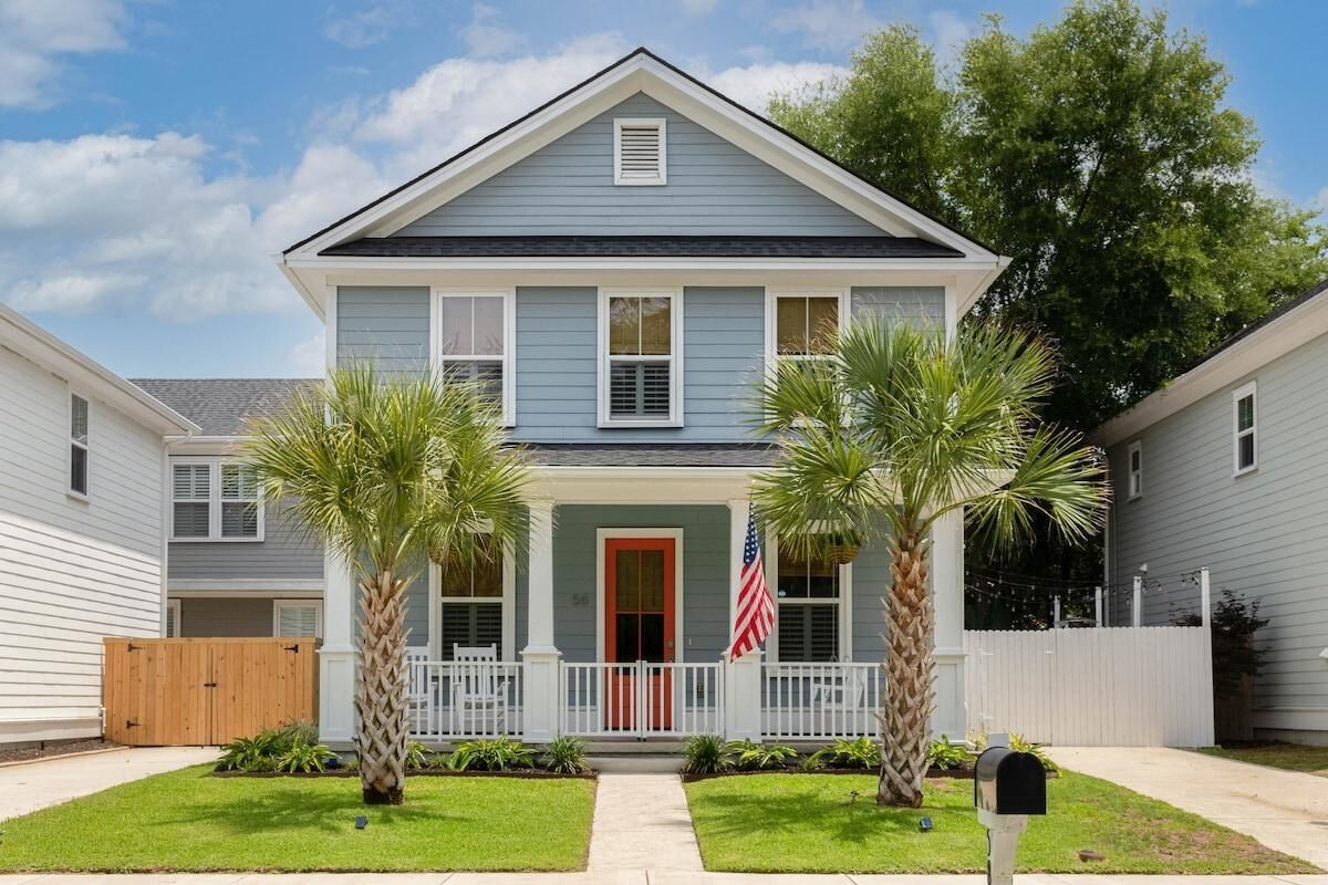 A two-story house with a front porch, a red door, and two palm trees.