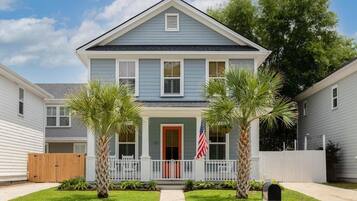 A two-story house with a front porch, a red door, and two palm trees.