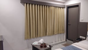 Habitació d'hotel amb un llit, una taula de nit amb productes de tocador, una porta i una finestra amb cortines.