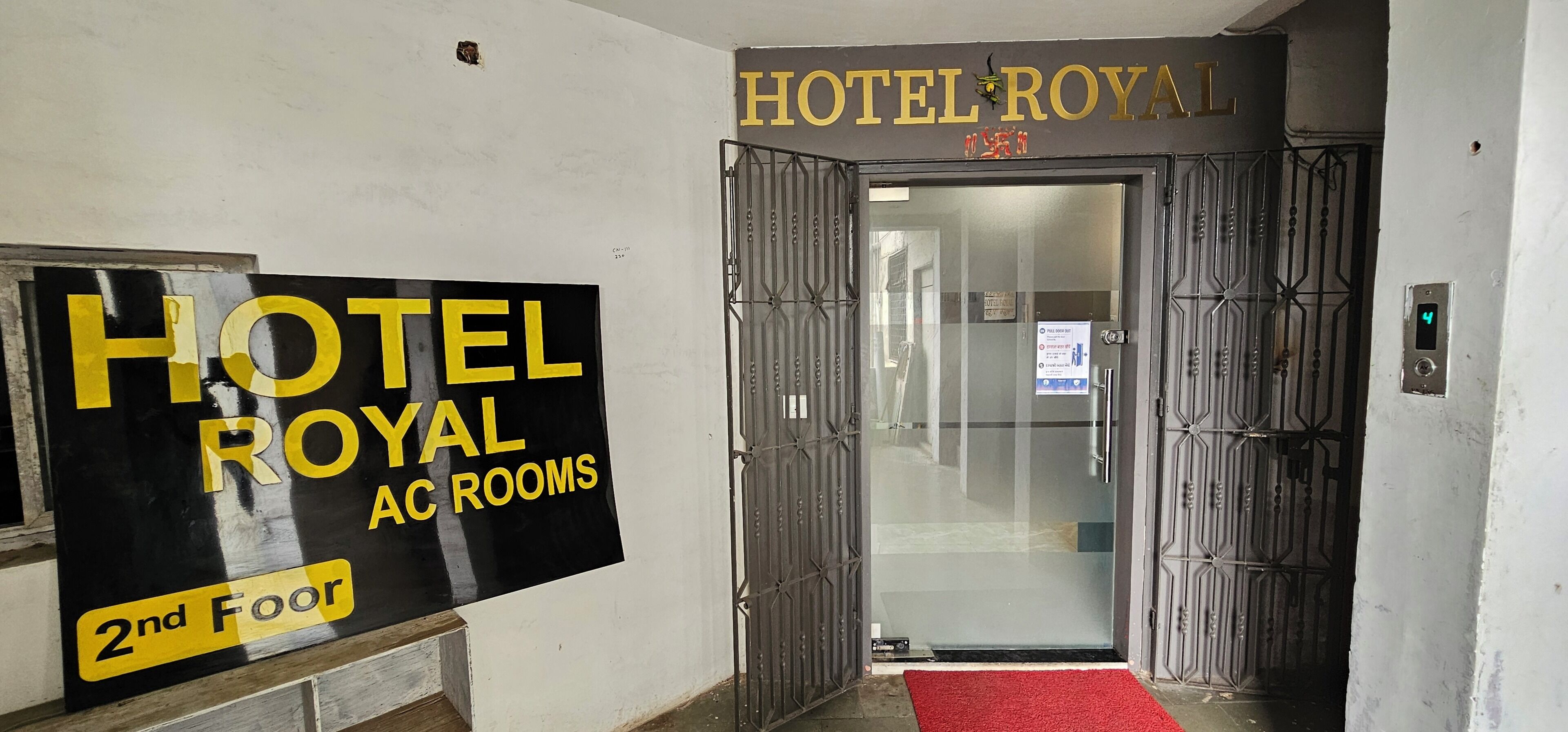 Una entrada de hotel con un cartel que dice 'HOTEL ROYAL AC ROOMS' en la pared y una alfombra roja que lleva a la puerta.