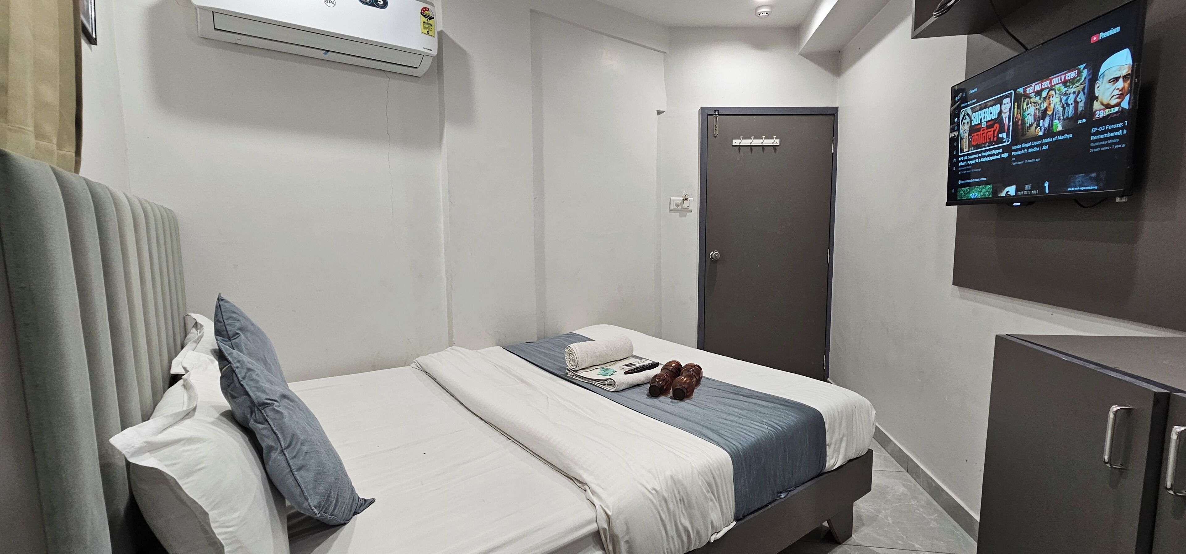 A hotel room with a bed, a television, a wardrobe, and a door.