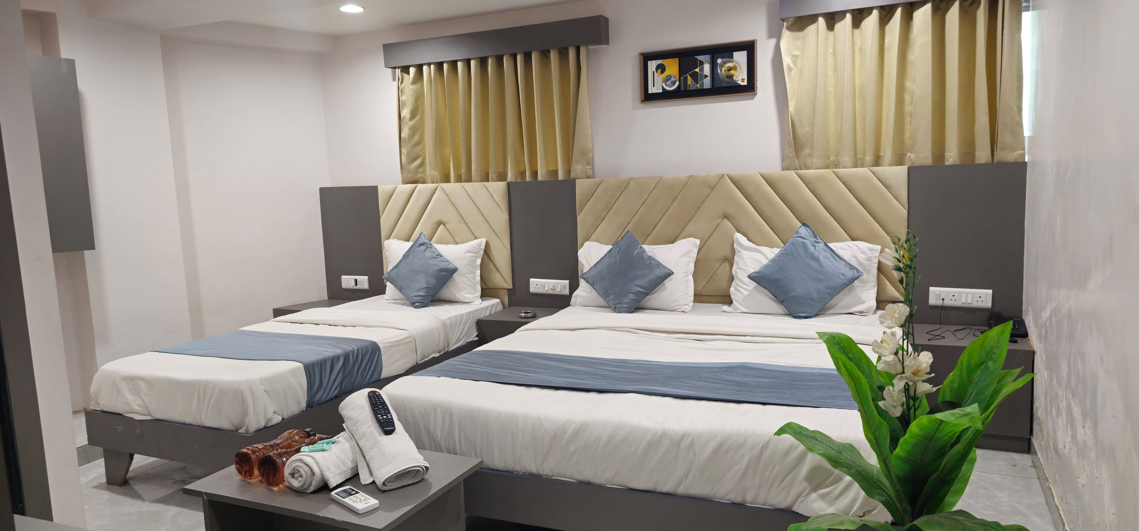 Een hotelkamer met twee bedden, een nachtkastje met een afstandsbediening, een plant en een stopcontact.