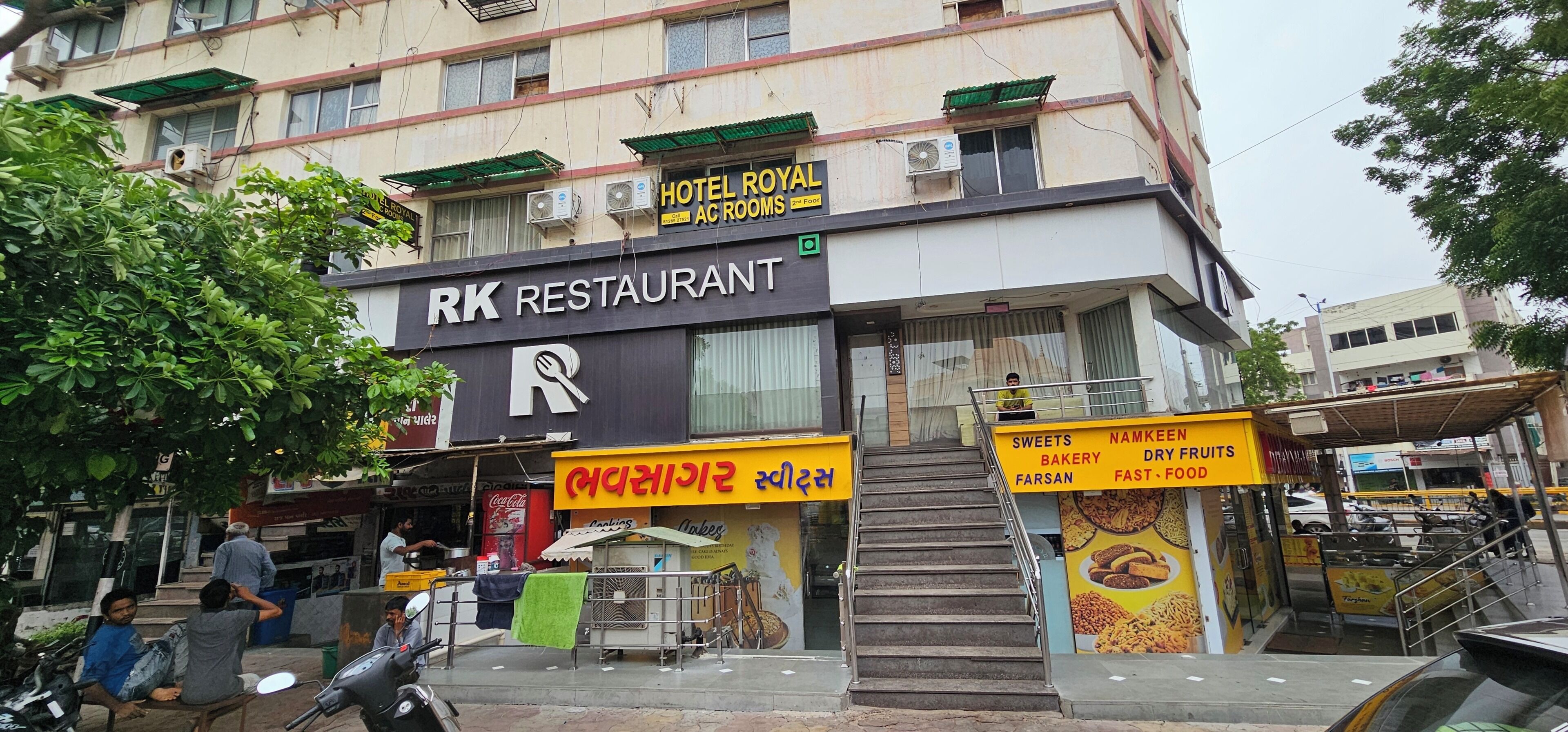 Een gebouw met een bordje 'RK Restaurant' en een trap die leidt naar een winkel met een bordje 'Sweets, Namkeen, Bakkerij, Fast Food'.