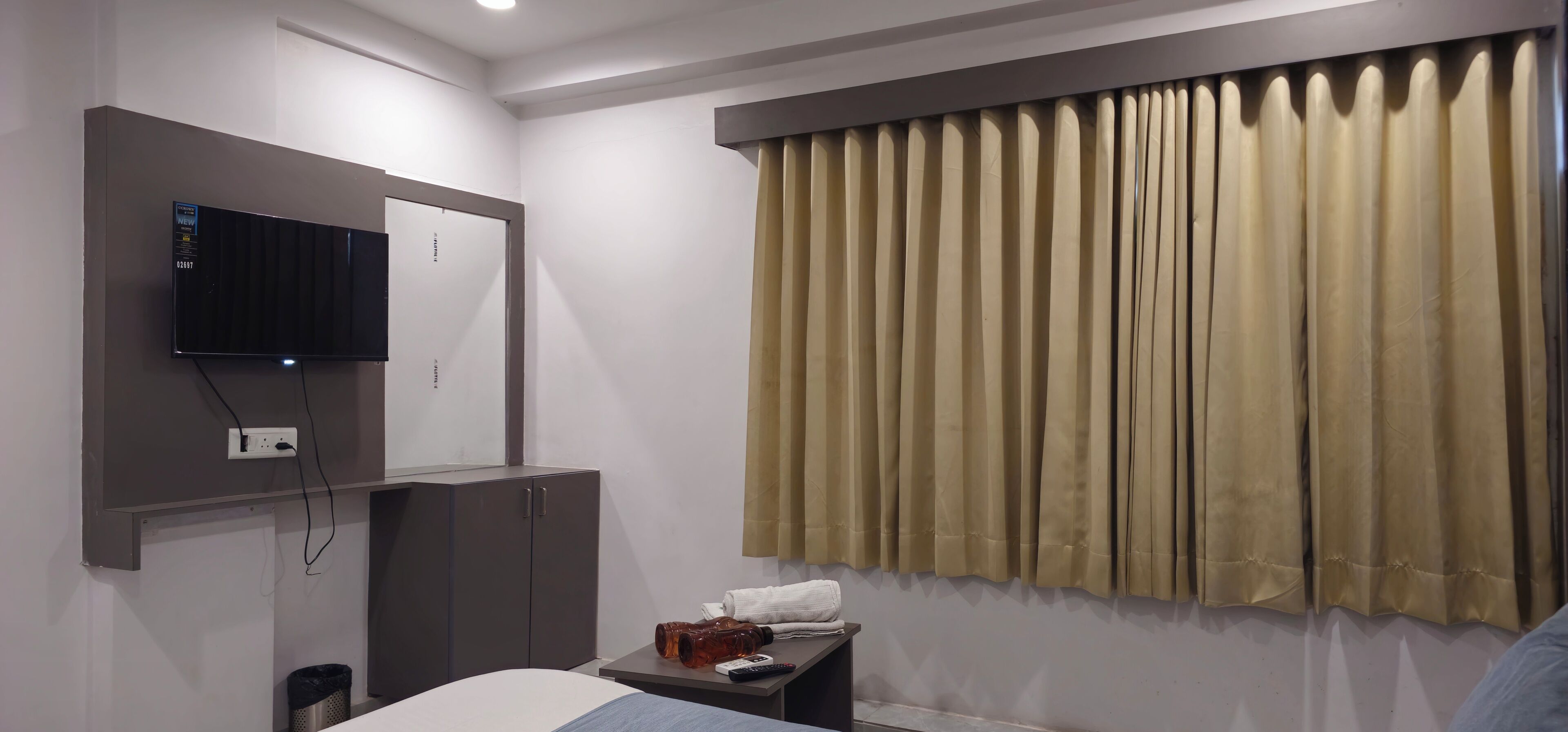 Quarto de hotel com cama, televisão na parede, uma mesinha com um controle remoto e janela com cortinas.