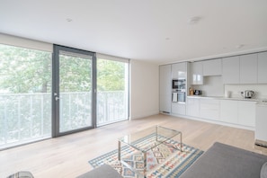 A modern kitchen with white cabinets, a glass-top coffee table, and a patterned rug. - 1BD City Retreat by the River Thames, Battersea (London)