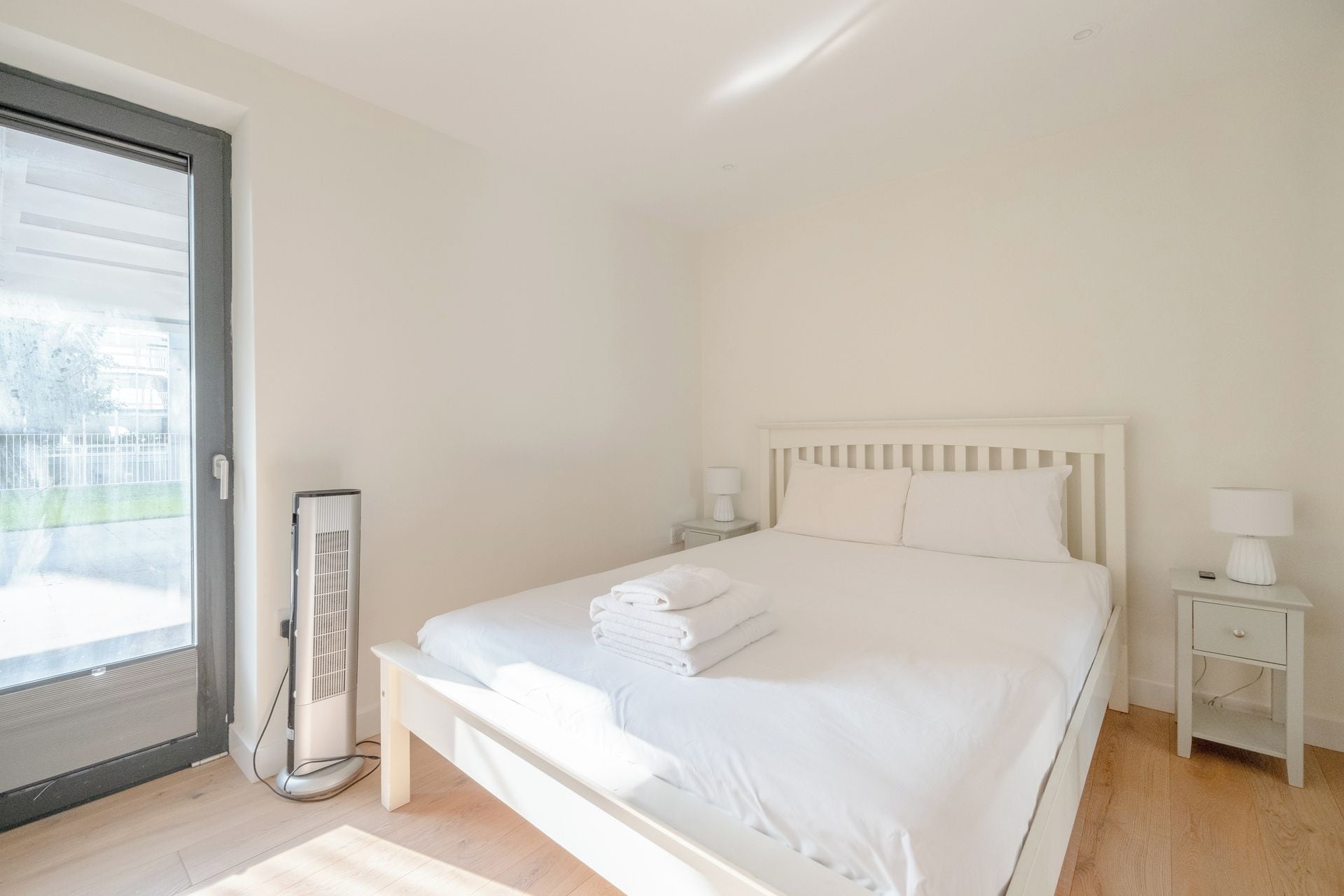 A bedroom with a bed, bedside tables, a heater, and a view through a glass door.