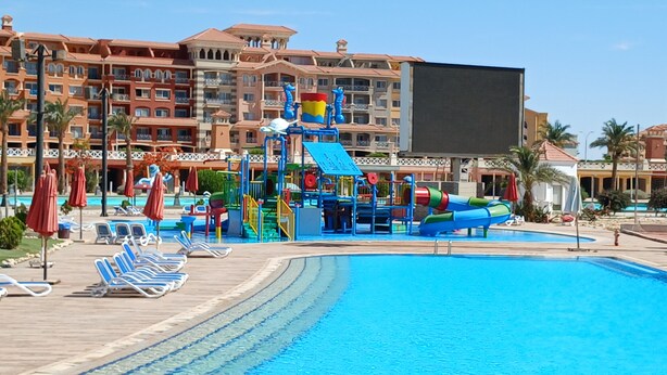 Ein Poolbereich eines Resorts mit Wasserrutsche, Liegestühlen und einem großen Gebäude im Hintergrund.