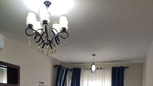 Ein Hotelzimmer mit einem Bett, einem Esstisch mit Stühlen, einer Deckenleuchte, einem Fernseher und Vorhängen.
