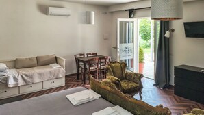 A room with a bed, a sofa, a dining table with chairs, a TV, and a sign indicating a camera rental service.