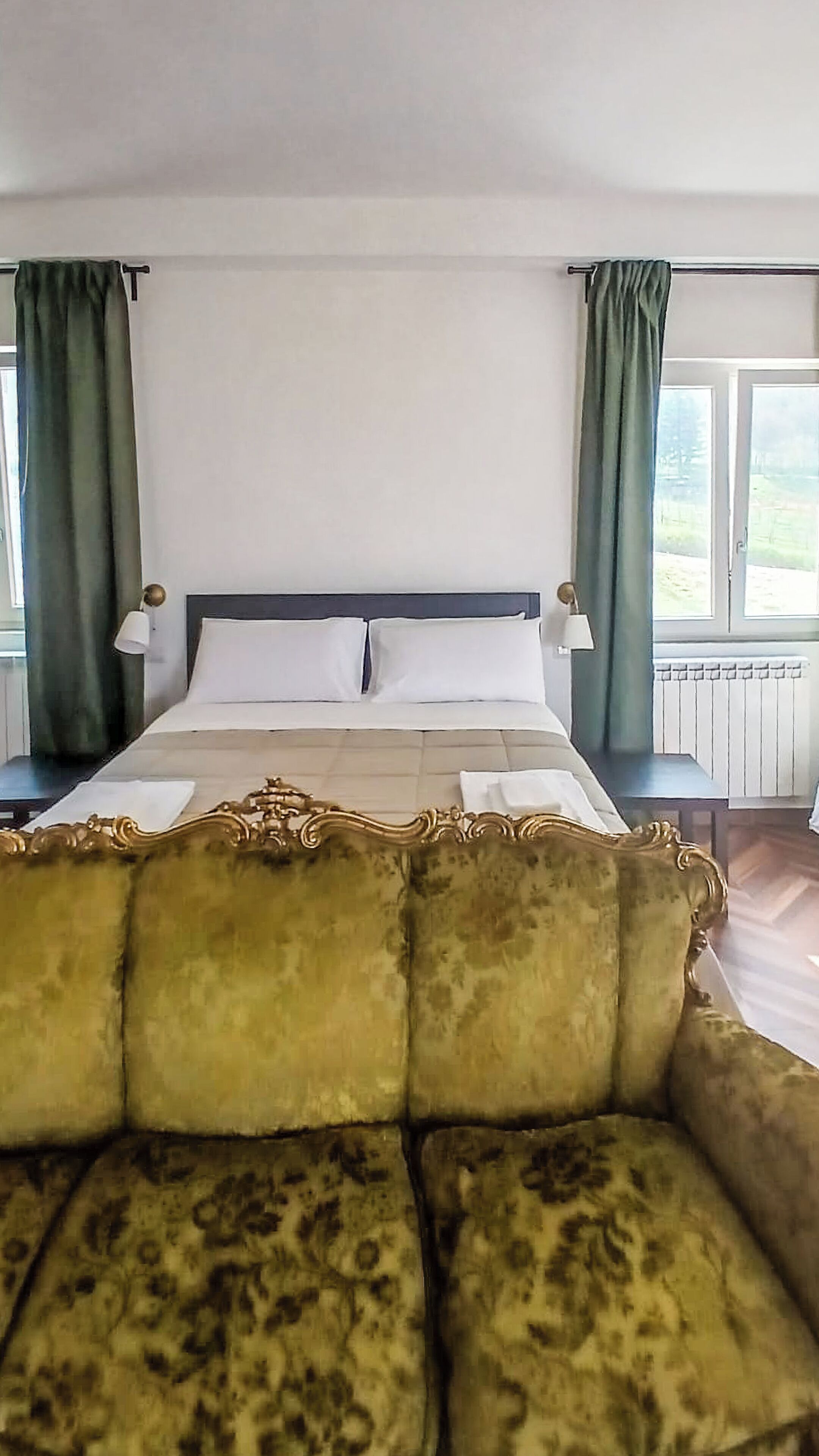Um quarto com uma cama, duas mesas de cabeceira, um sofá e vista para o exterior pela janela.