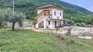 A two-story house with a balcony, a car parked in front, and a mountainous backdrop.