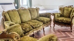 A room with a large sectional sofa, a matching armchair, a patterned rug, and a window with curtains.
