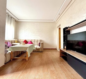 A living room with a sofa, a coffee table, a flat-screen TV, and a wooden floor.