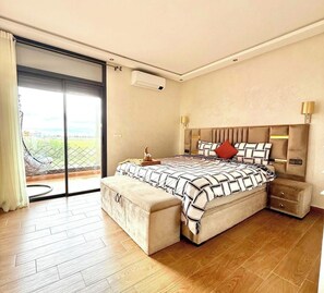 A bedroom with a large bed, a sliding glass door to a balcony, a wall-mounted air conditioner, and a bedside lamp. - Cosy villafor your stay (Marrakech)
