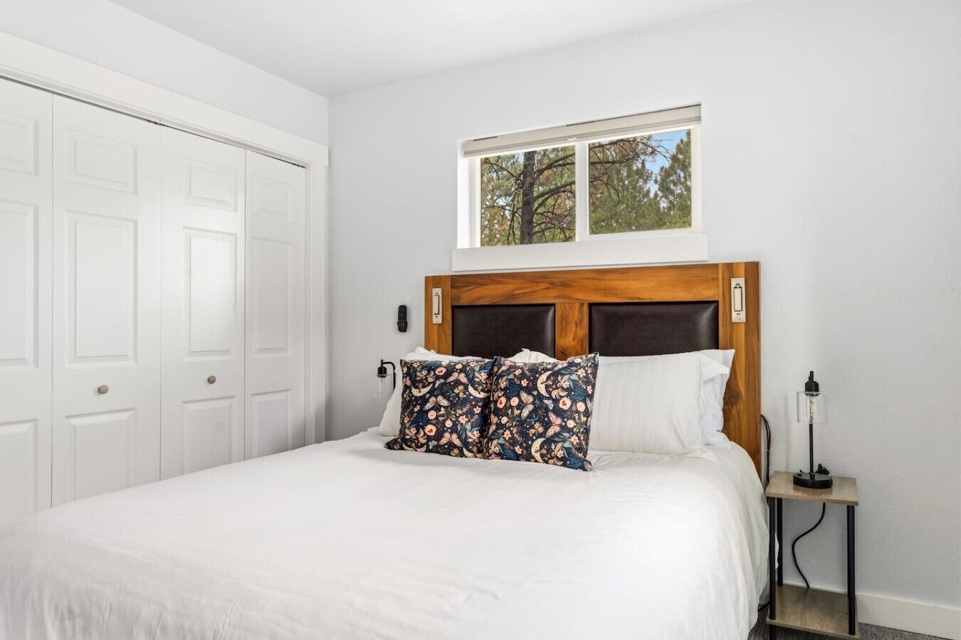 A bedroom with a large bed, a wooden headboard, a window, and a bedside table with a lamp.