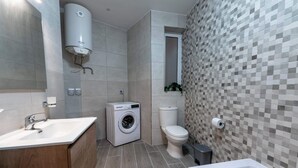 A modern bathroom with a built-in washing machine, a toilet, and a bathtub.