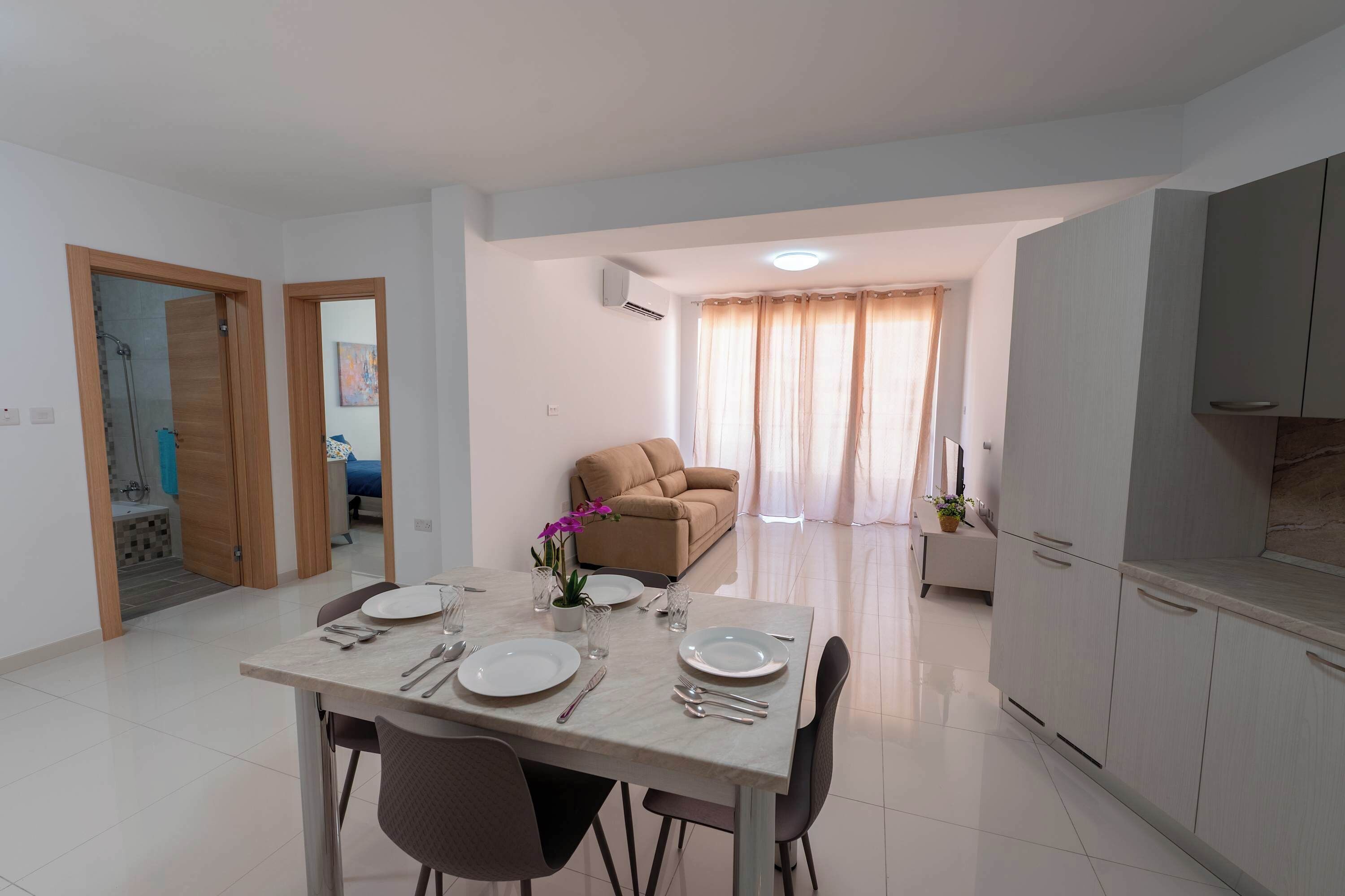 A dining area with a table set for four, a sofa, and a kitchen area with cabinets.