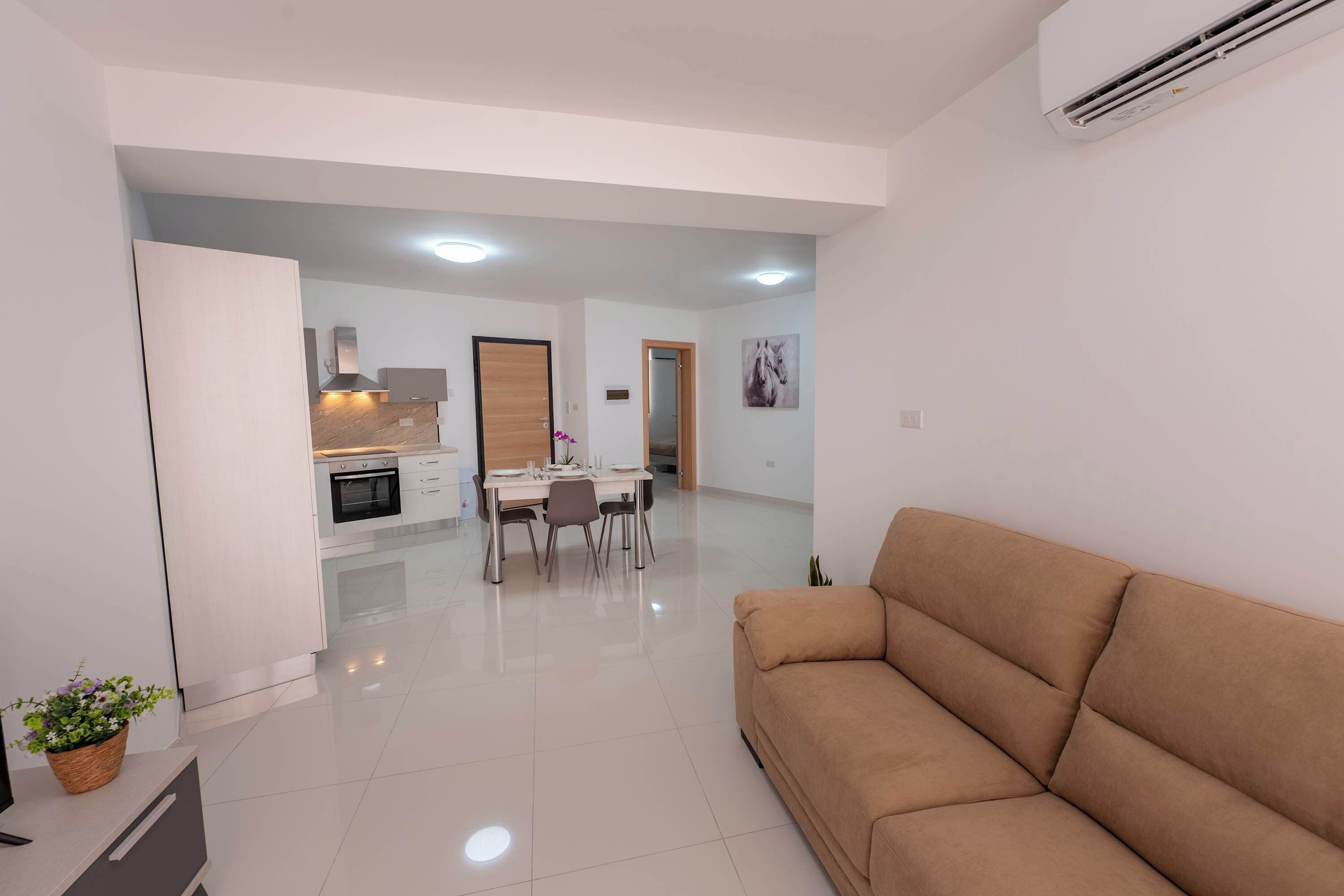 A modern living room with a sofa, a dining area with chairs and a table, and a kitchen in the background.
