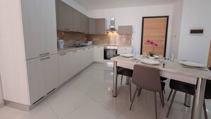 A modern kitchen with white cabinets, a built-in oven, and a dining area with a table set for four.