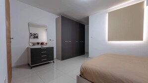A bedroom with a bed, a dresser, a wardrobe, a mirror, and a wall-mounted light fixture.