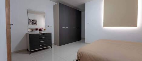 Une chambre à coucher comprenant un lit, une commode, une armoire, un miroir et un luminaire fixé au mur.