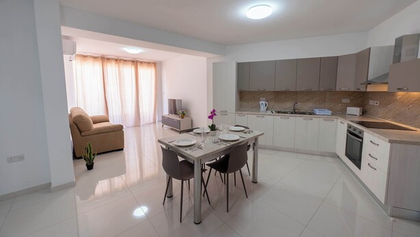 A modern kitchen with white cabinets, a dining table set for four, and a built-in oven.