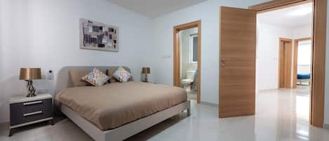 A bedroom with a bed, bedside tables, a wall-mounted artwork, and an open door leading to another room.